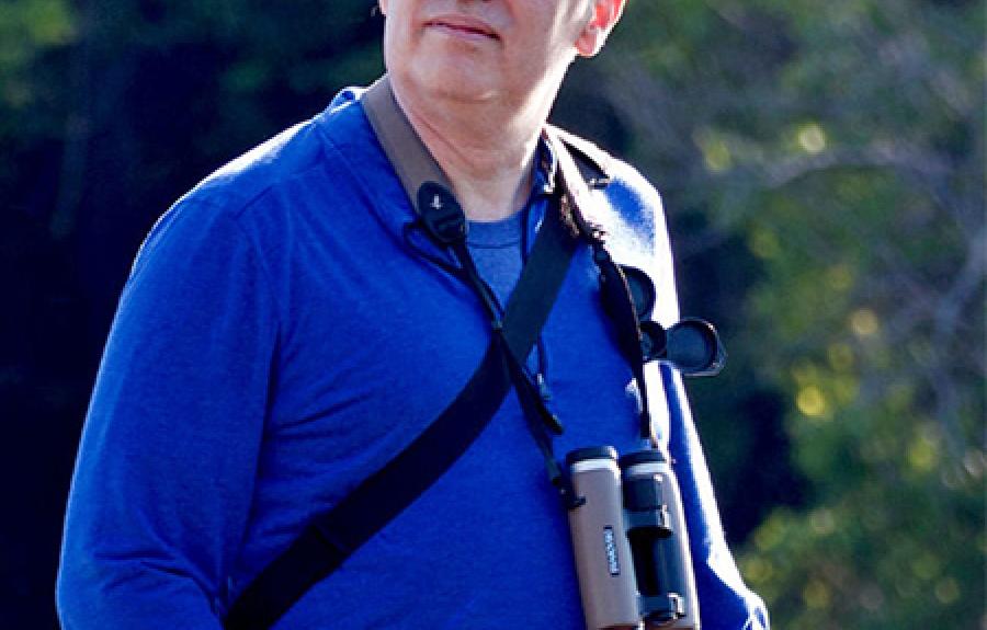 A portrait of Ian Owens wearing binoculars