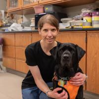 A portrait of Hannah DeFelice with a black labrador retriever dog.